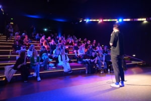 Das Publikum hört gespannt dem Moderator auf der Bühne zu