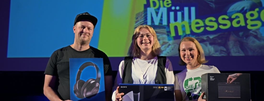 Die drei Finalist*innen des Poetry Slams "Die Müll Message" auf dem Heldenmarkt Berlin stehen auf der Bühne und halten ihre Preise in den Händen.