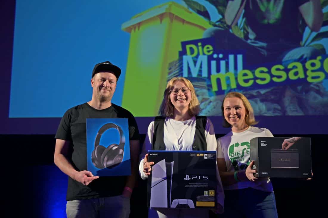 Die drei Finalist*innen des Poetry Slams "Die M&uuml;ll Message" auf dem Heldenmarkt Berlin stehen auf der B&uuml;hne und halten ihre Preise in den H&auml;nden.